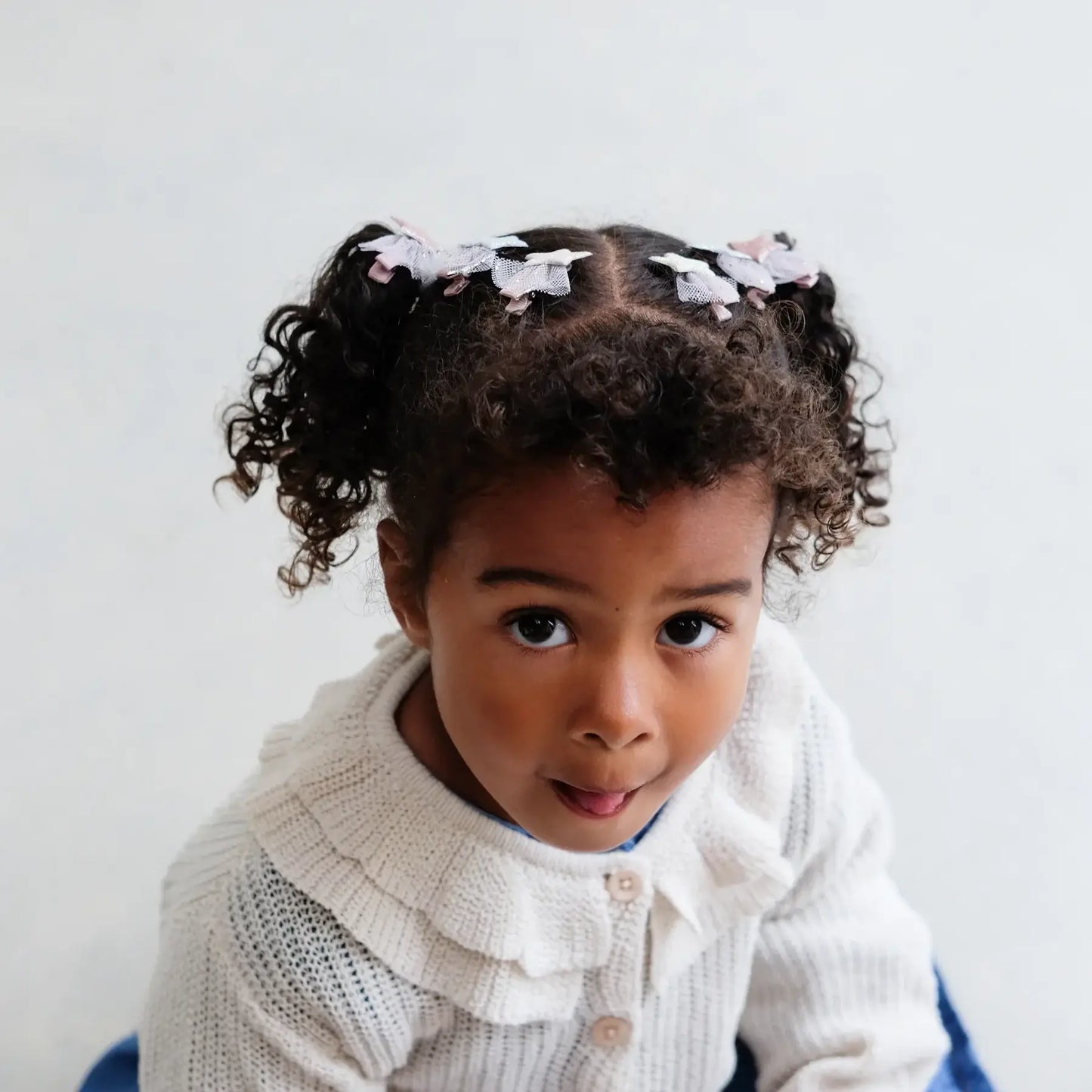 Girl with curly hair wearing Mimi & Lula ballet star mini clips, smiling playfully in a cozy sweater.
