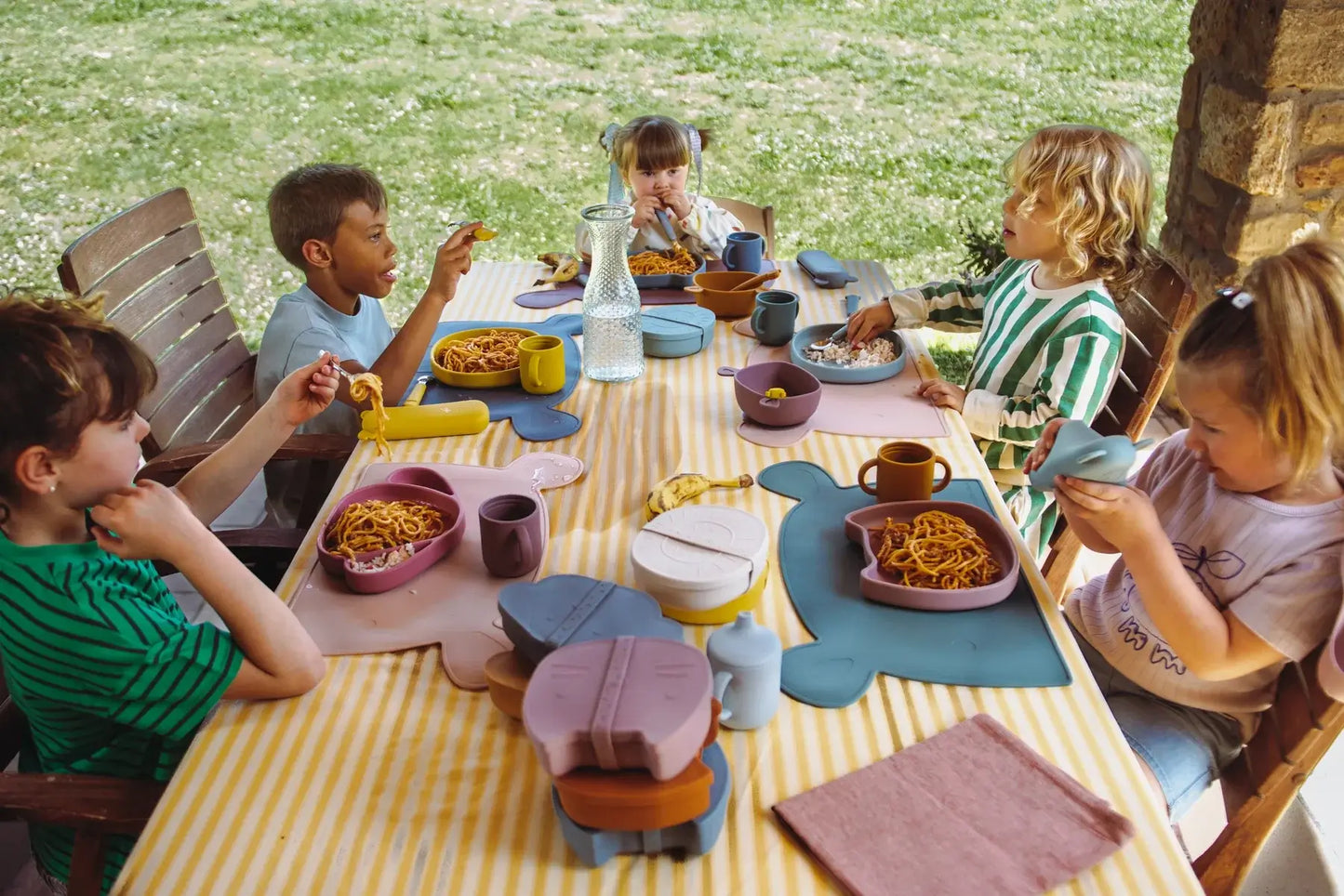 Kids enjoying a colorful outdoor meal with playful tableware on a sunny day.