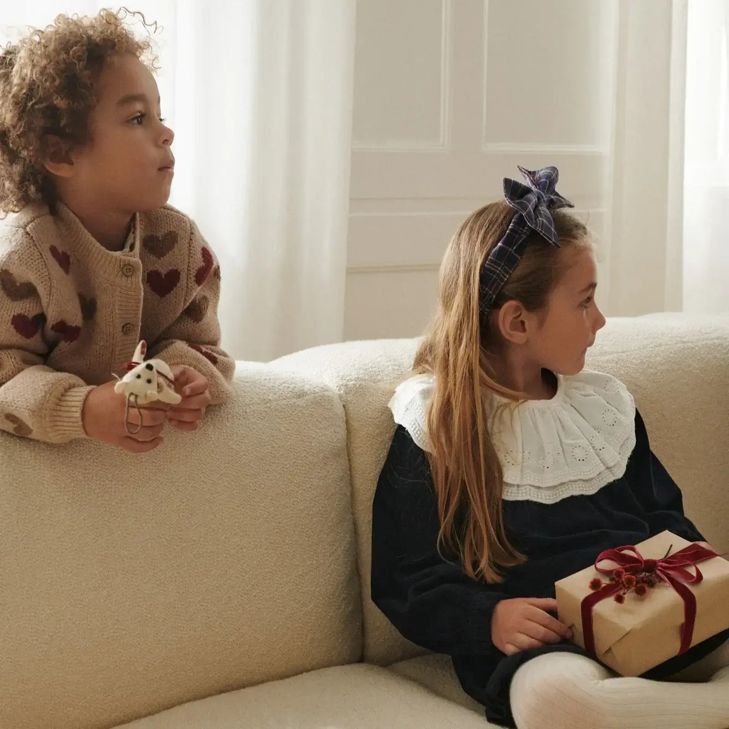 Kids wearing cozy Wheat sweaters, one with hearts and the other in a classic collar, posing with gifts.