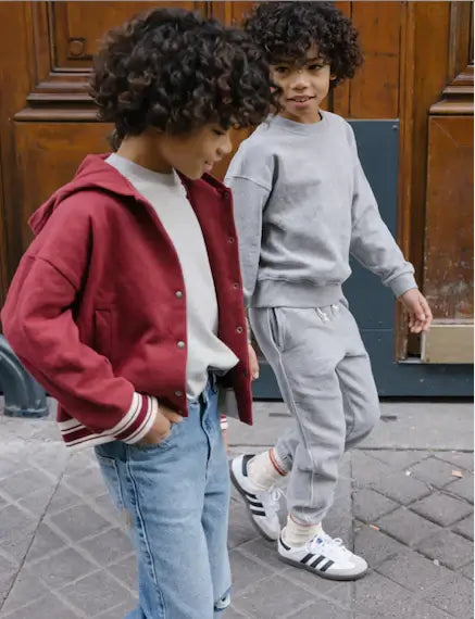 Two children walking on a street, one in a red jacket and the other in grey sweatpants, showcasing trendy kids' fashion.