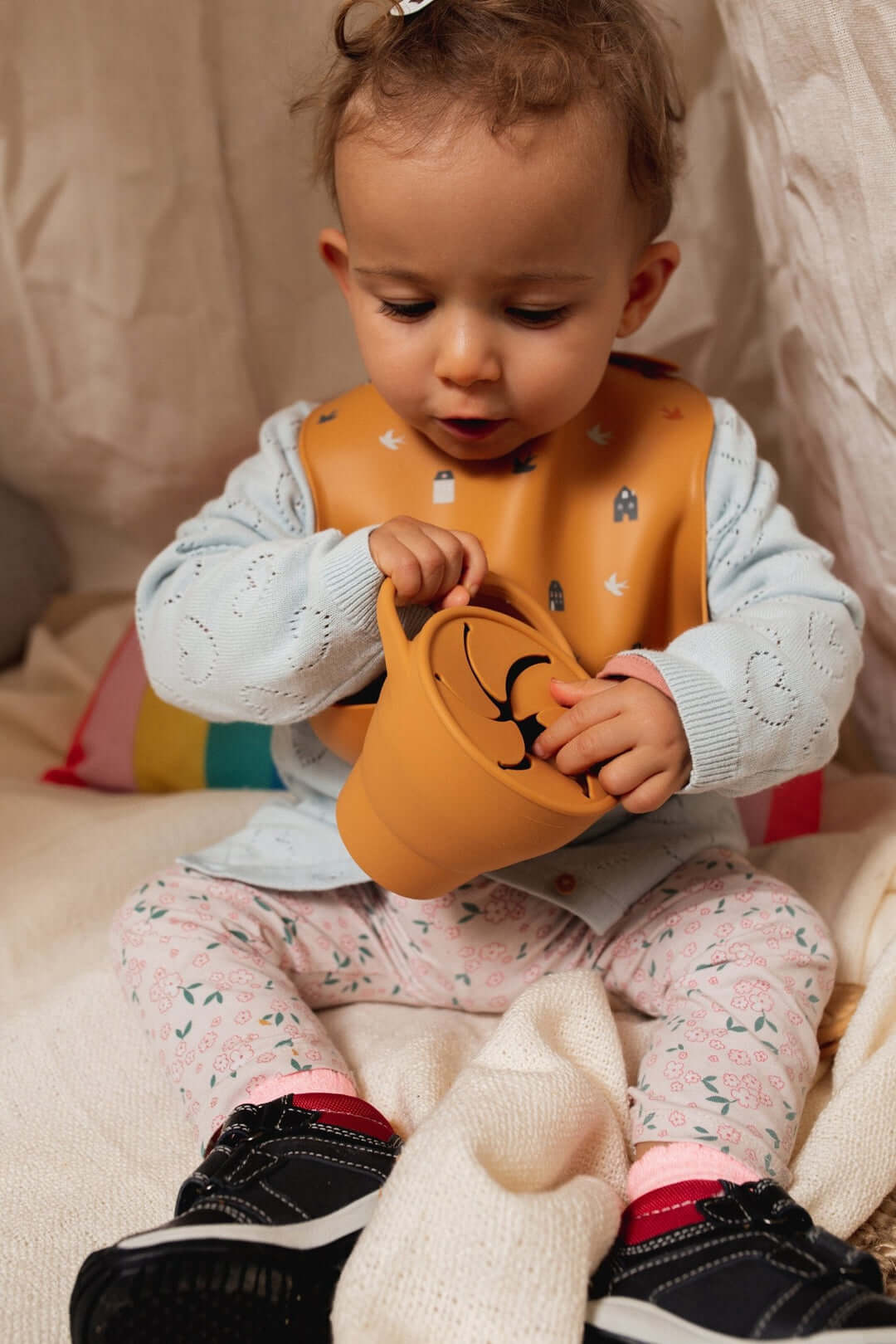 Baby wearing a Cotton Cloud bib, happily playing with a toy cup in a cozy indoor setting.