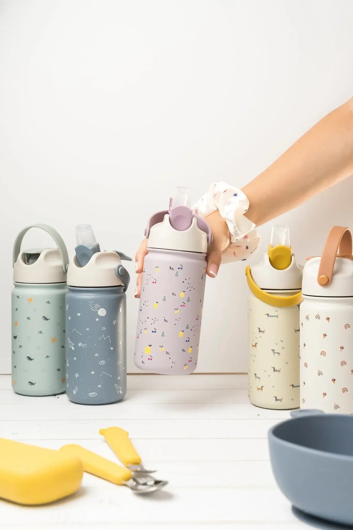 Hand holding a colorful stainless steel drink bottle among five stylish options for kids' hydration.