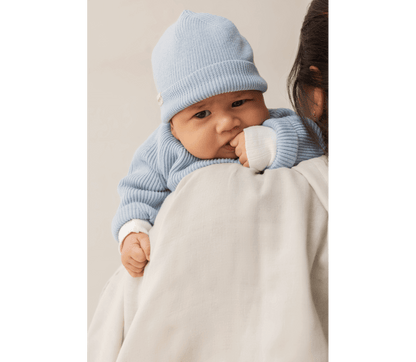 Newborn in a soft blue MarMar Copenhagen knitted hat, comfortably resting on a caregiver's shoulder.