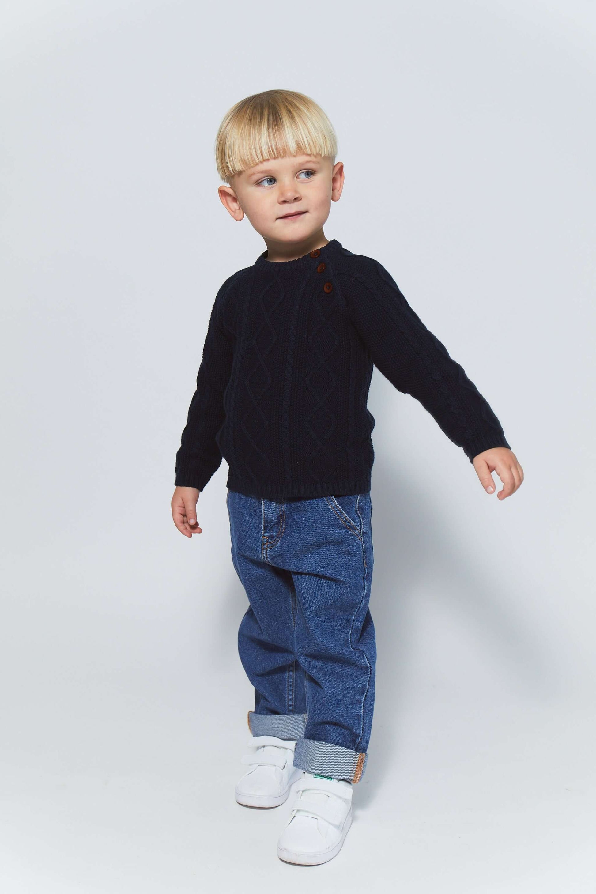 Kind in een navy blauwe gebreide kabeltrui van Copenhagen Colors, gecombineerd met denim broek en sneakers.