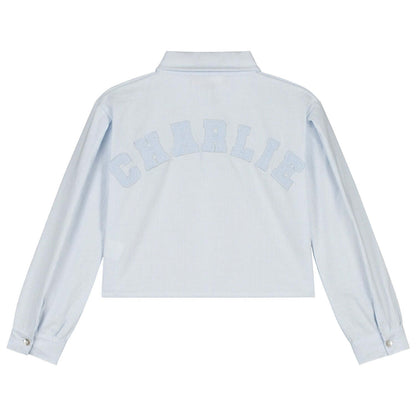 Back view of Charlie Petite Gaby Blouse in light blue with white lettering, perfect for stylish girls' fashion.