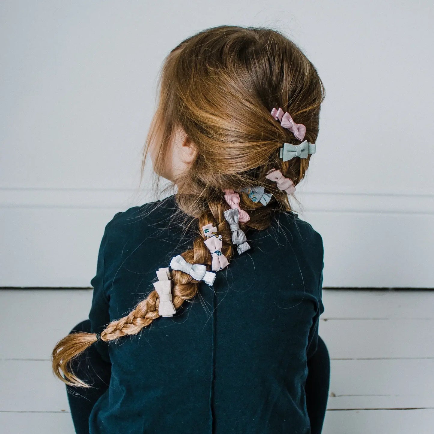 Girl with braided hair adorned by colorful Mimi & Lula Martha mini bow clips in soft pink and gray tones.