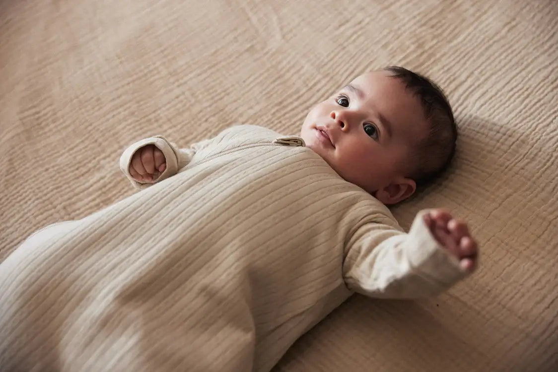 Baby in a cozy beige sleep sack, enjoying a comfy moment on soft bedding, perfect for a stylish nap.