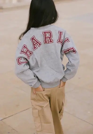 Child wearing a grey melange Charlie sweater with bold lettering, paired with stylish beige cargo pants.