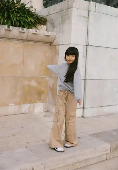 Young girl wearing a stylish grey melange Jones Sweater and beige cargo pants, posing outdoors.